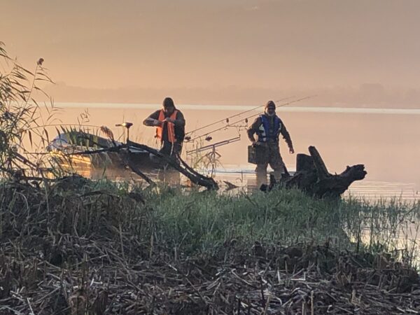 Due carpisti con le canne in azione all'alba sulla riva del lago