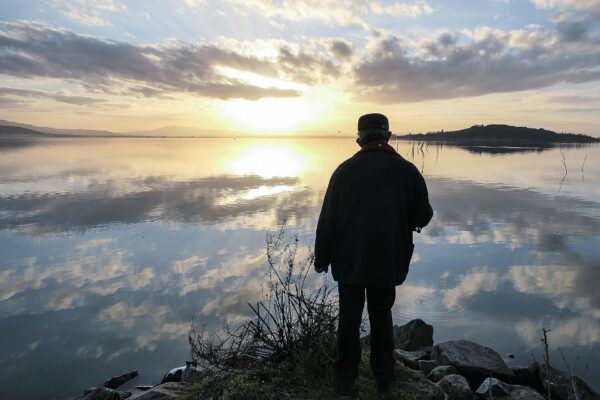 Pescatore con la canna al tramonto sulla riva di un lago
